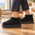 Person wearing black low ankle boots with a thick platform sole and rear pull tab, paired with dark cropped jeans on a wooden floor._0