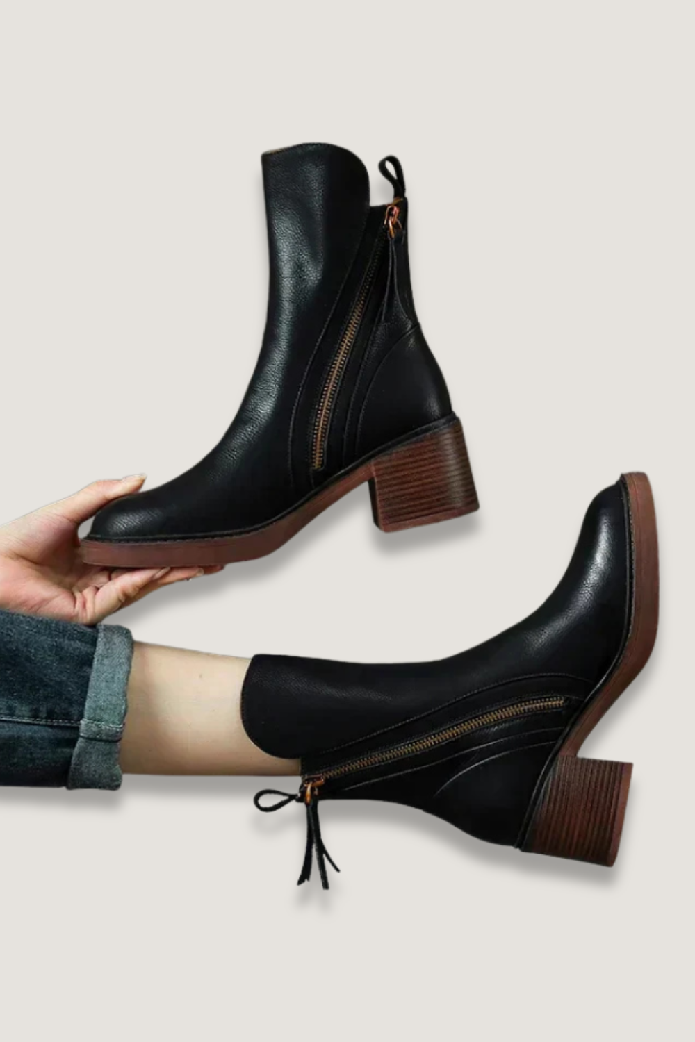 Pair of black ankle boots with side zips, pull tabs, pointed toes, and brown block heels, shown one held above the other.