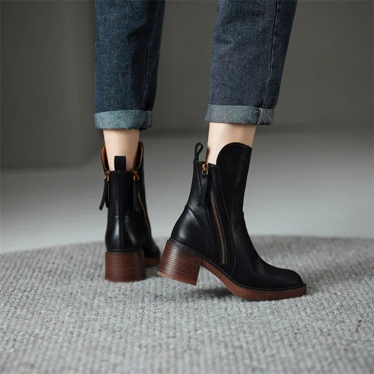 Back and side view of black ankle boots worn with cuffed jeans, showing the ankle-height shafts, pull tabs, side zip, and block heels.