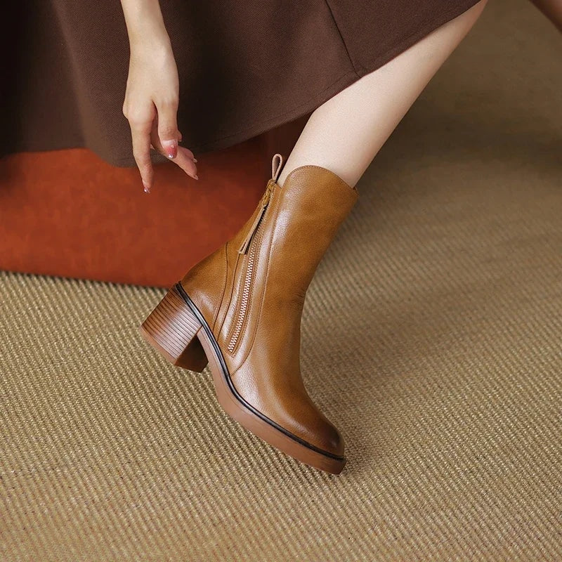 Close side view of a tan ankle boot beneath a brown skirt, emphasizing the side zipper, pointed toe, and stacked block heel.