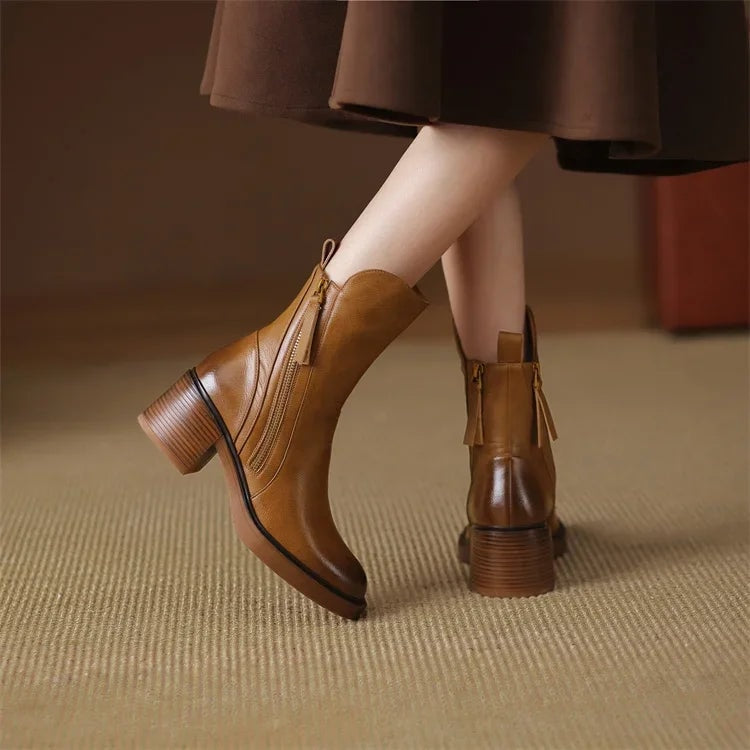 Tan ankle boots worn beneath a dark skirt, showing one boot from the rear and the other in side profile with side zips and block heels.