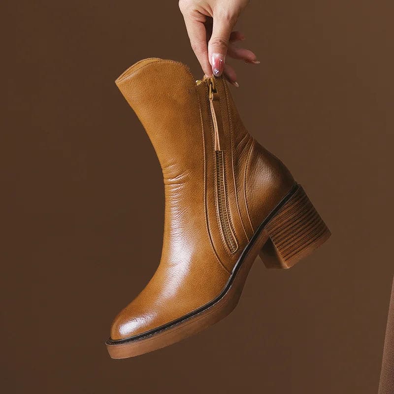 A hand holding a tan ankle boot by the zipper pull, showcasing the side zipper closure and block heel design._0