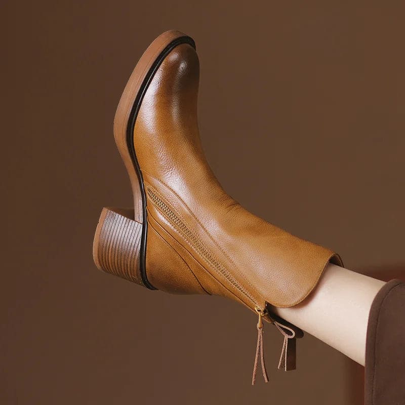 A hand holding a tan ankle boot by the zipper pull, showcasing the side zipper closure and block heel design._1