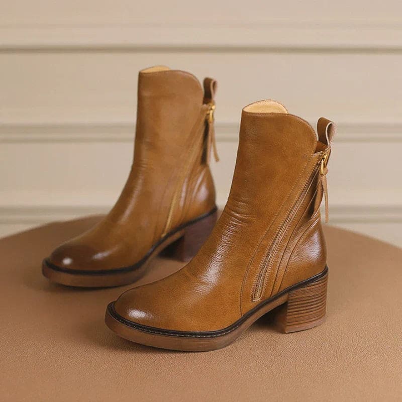 A hand holding a tan ankle boot by the zipper pull, showcasing the side zipper closure and block heel design._3