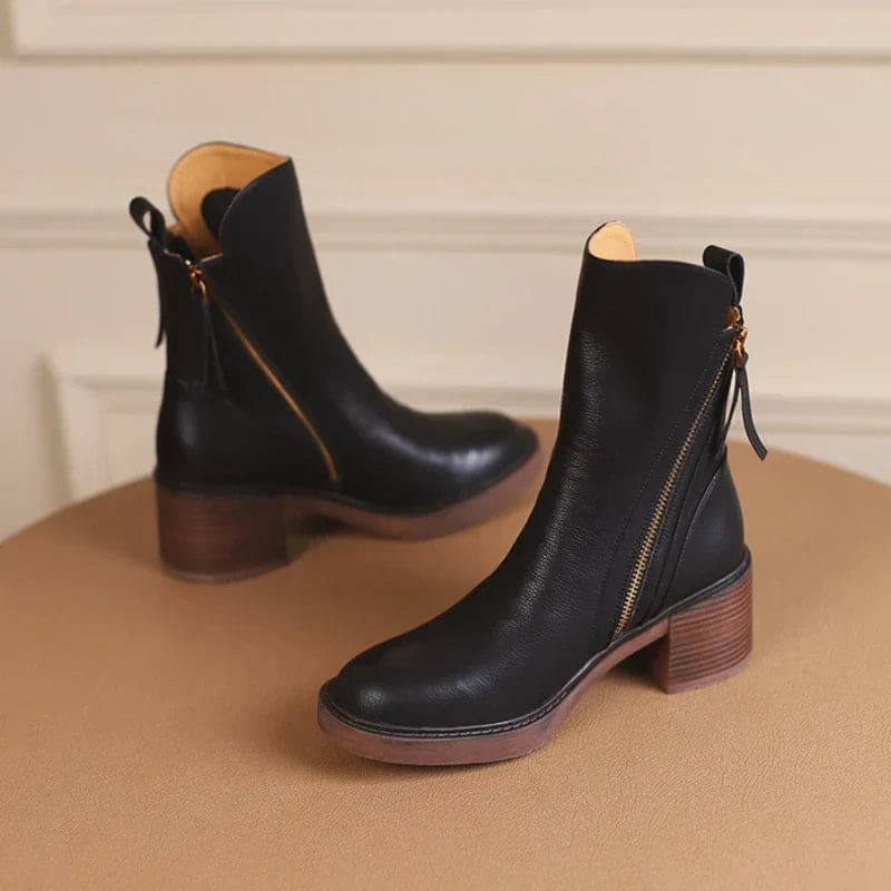A hand holding a tan ankle boot by the zipper pull, showcasing the side zipper closure and block heel design._4