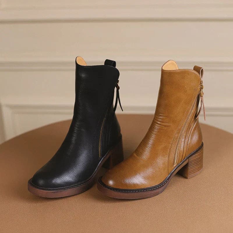 A hand holding a tan ankle boot by the zipper pull, showcasing the side zipper closure and block heel design._5