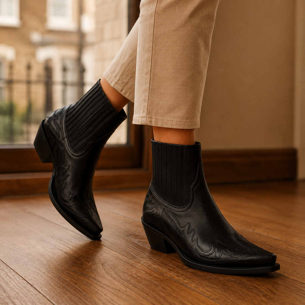Black pointed-toe western ankle boots with block heel, elastic side panels and tonal stitching, worn with beige cropped trousers on a wooden floor._0