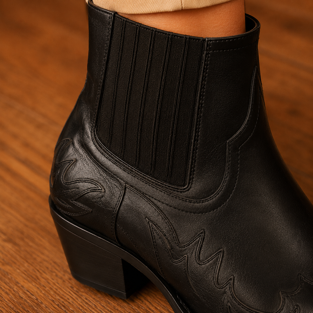 Black pointed-toe western ankle boots with block heel, elastic side panels and tonal stitching, worn with beige cropped trousers on a wooden floor._1