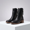 Pair of black mid-calf boots with gold side zips, brown stacked block heels and rounded toes on a white plinth._0