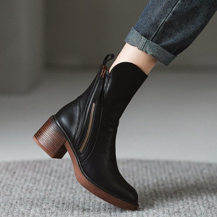 Pair of black mid-calf boots with gold side zips, brown stacked block heels and rounded toes on a white plinth._4