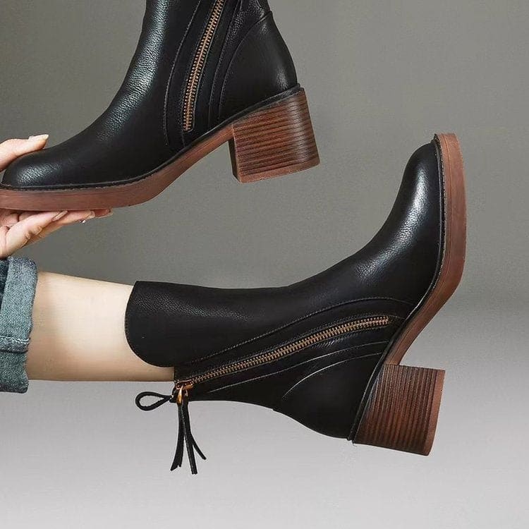 Pair of black mid-calf boots with gold side zips, brown stacked block heels and rounded toes on a white plinth._5