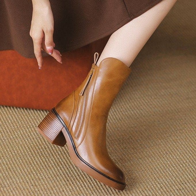 Pair of black mid-calf boots with gold side zips, brown stacked block heels and rounded toes on a white plinth._6