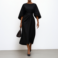 Woman wearing an ankle-length belted dress with wide dolman sleeves in a minimalist setting_0