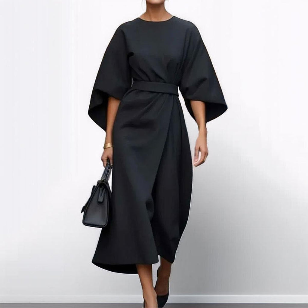 Woman wearing an ankle-length belted dress with wide dolman sleeves in a minimalist setting_2