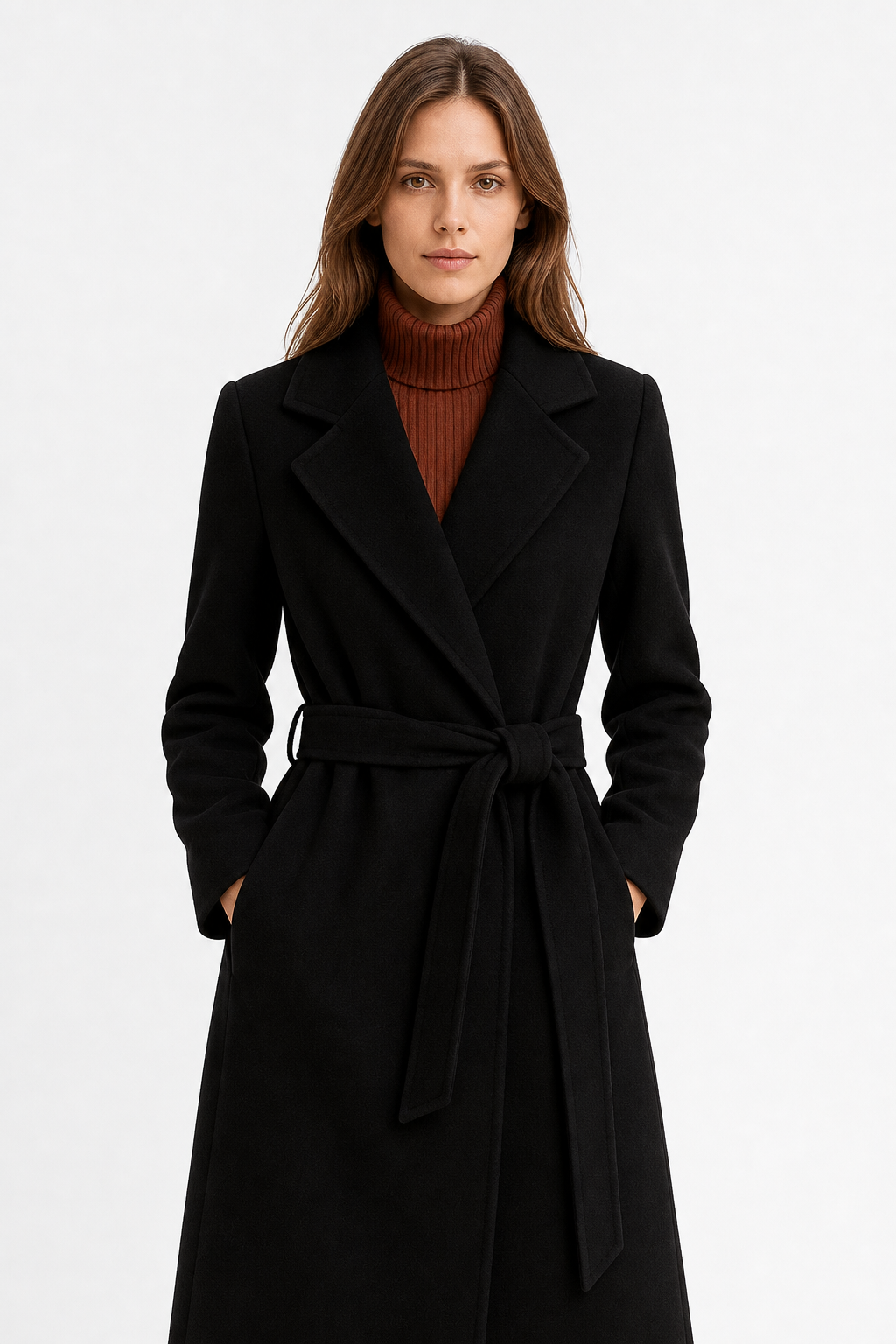Woman wearing a camel belted midi coat with tie waist over a turtleneck and black trousers, standing in natural light._11