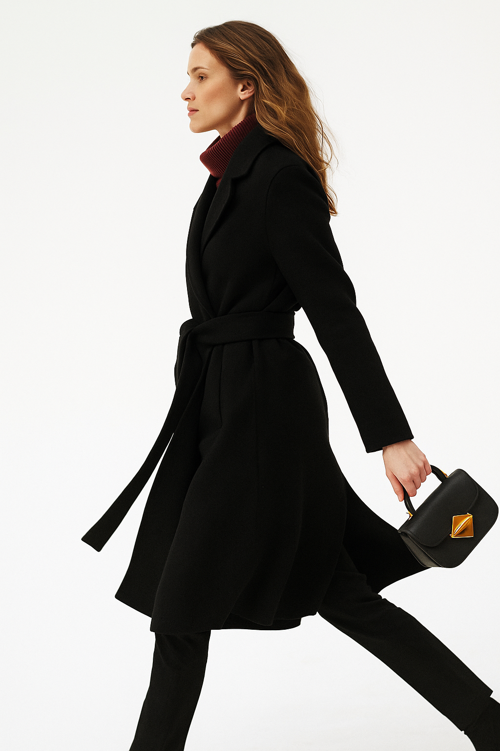 Woman wearing a camel belted midi coat with tie waist over a turtleneck and black trousers, standing in natural light._20