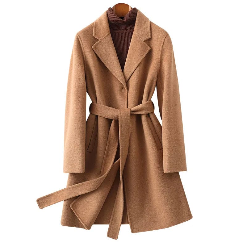 Woman wearing a camel belted midi coat with tie waist over a turtleneck and black trousers, standing in natural light._29