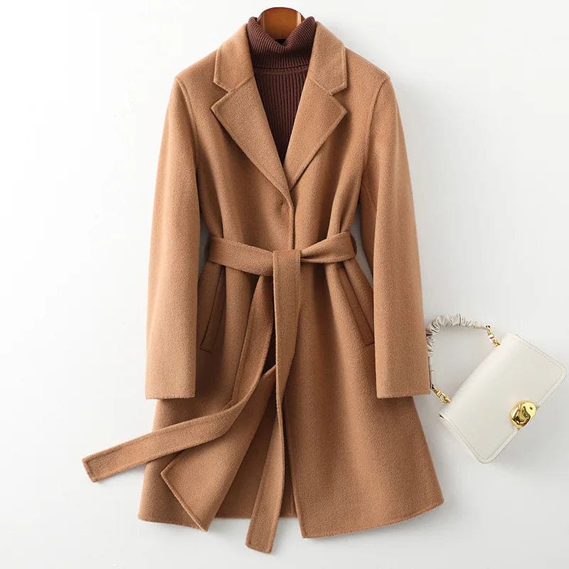 Woman wearing a camel belted midi coat with tie waist over a turtleneck and black trousers, standing in natural light._30