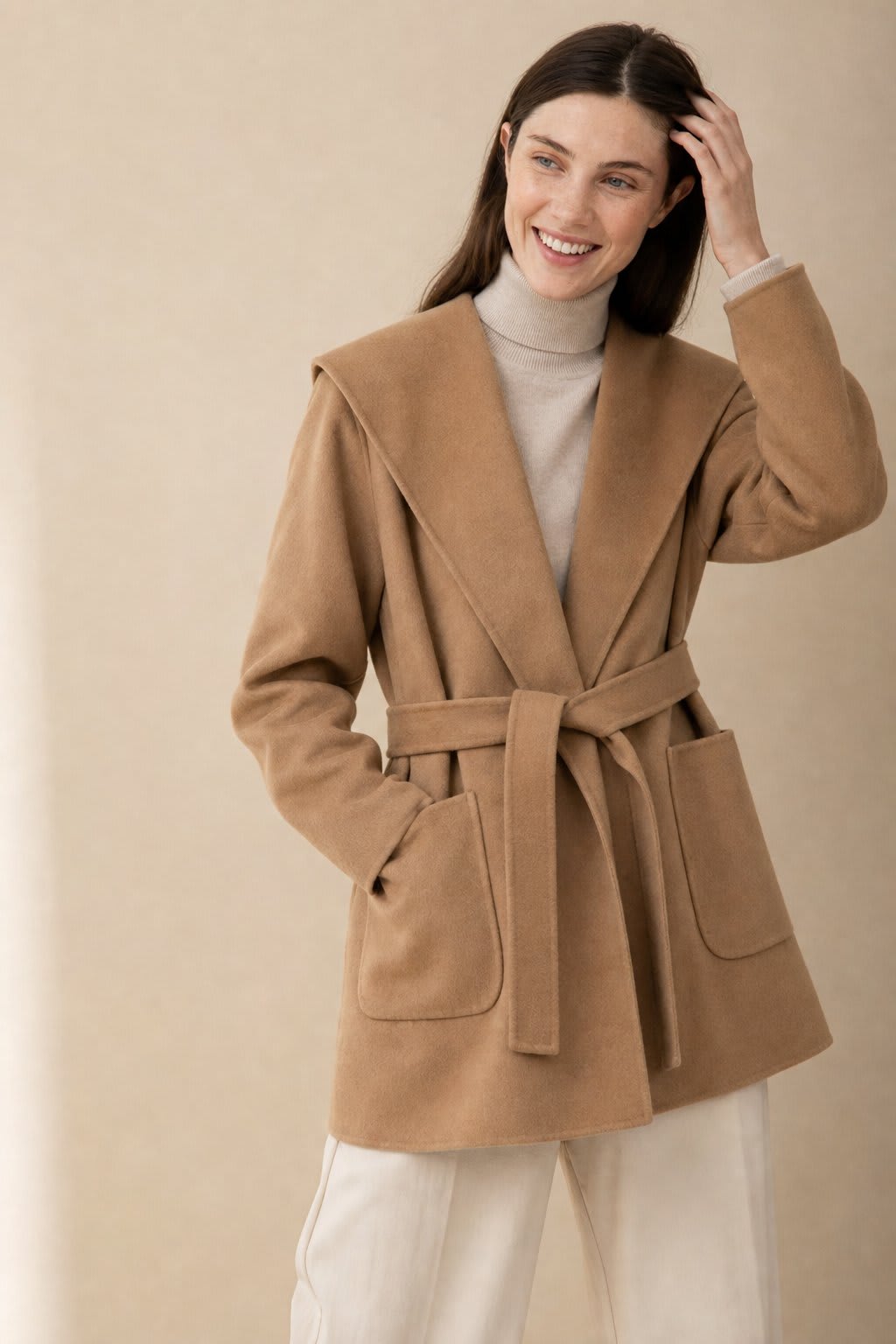 Woman wearing a belted wrap coat with a wide shawl collar, tie belt, and patch pockets over a turtleneck and trousers._0