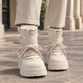Cream ankle boots with drawstring padded cuff, instep strap, thick laces and chunky platform lug sole worn with light beige jeans on a paved street._0