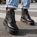Person wearing black platform ankle boots with front zips and laces, styled with cuffed light blue jeans on a street crossing._0