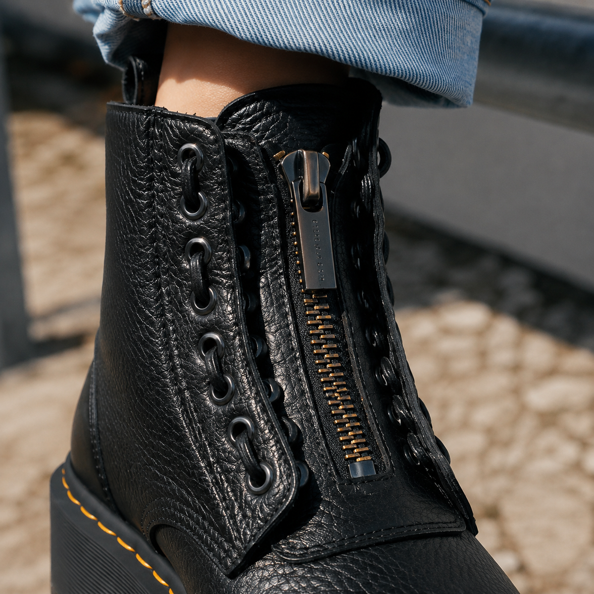 Person wearing black platform ankle boots with front zips and laces, styled with cuffed light blue jeans on a street crossing._2