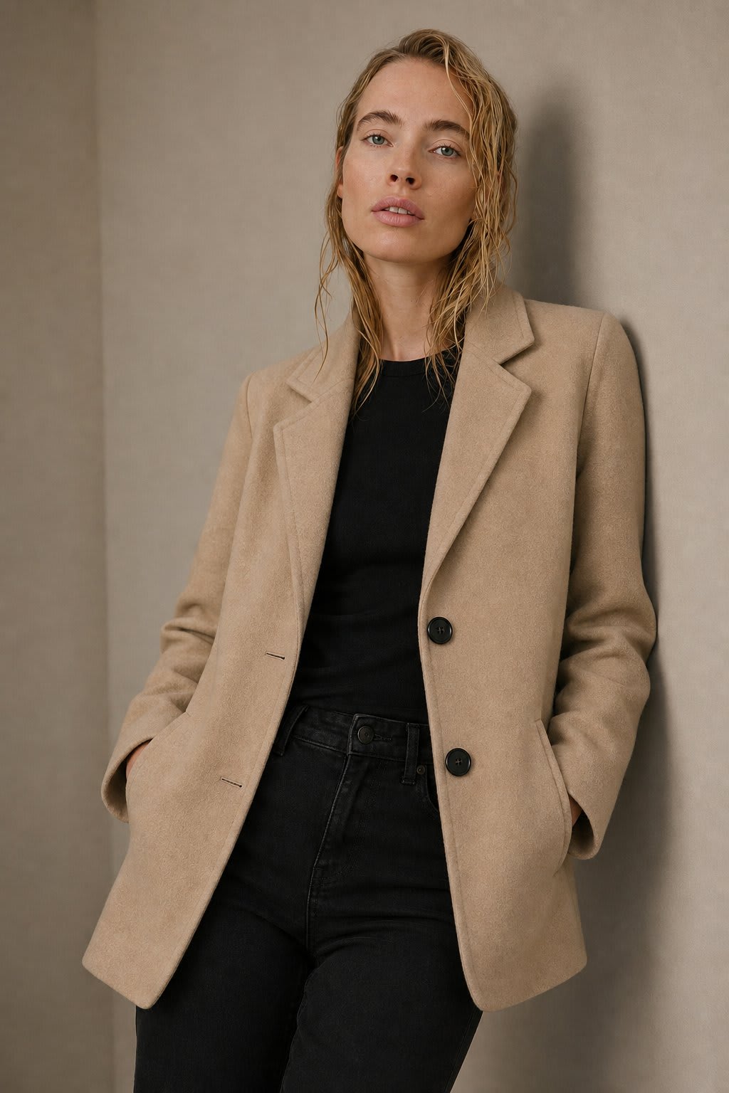 Woman wearing a beige blazer over a black top with dark jeans against a neutral background_0