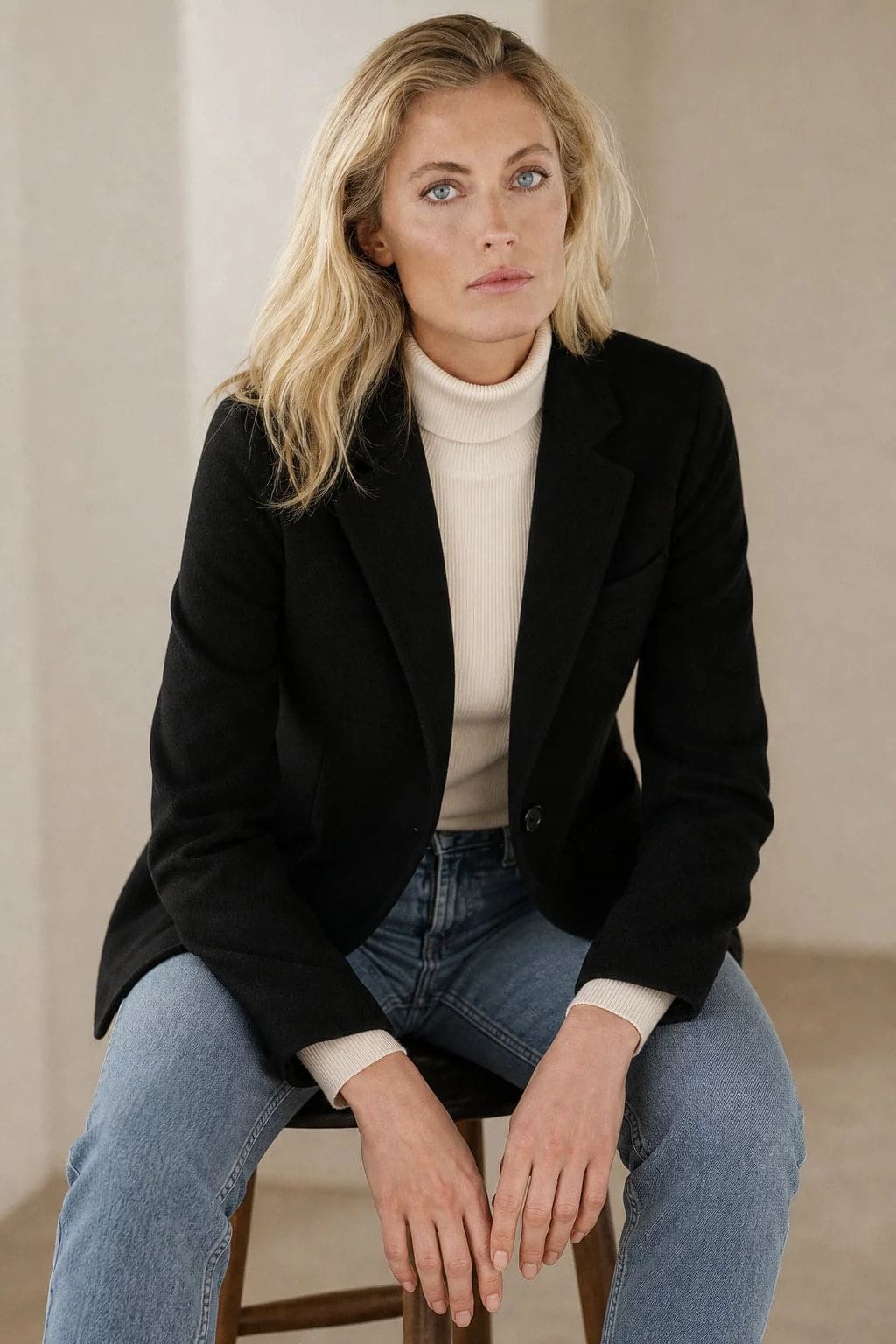 Woman wearing a beige blazer over a black top with dark jeans against a neutral background_3