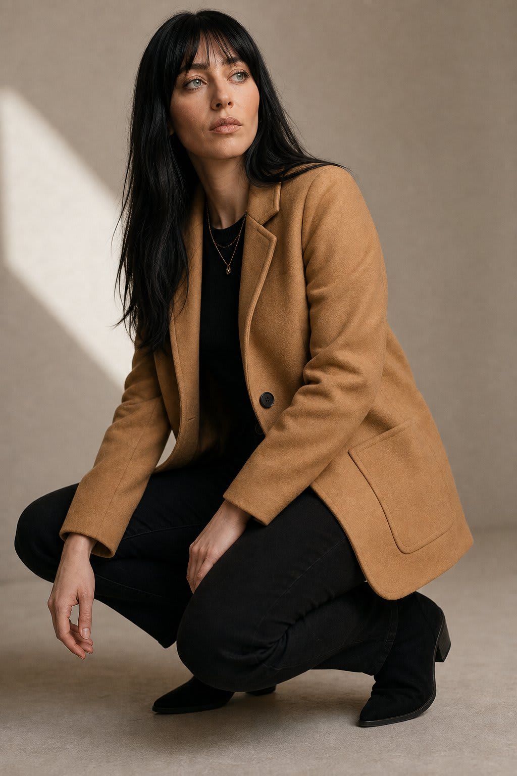 Woman wearing a beige blazer over a black top with dark jeans against a neutral background_4