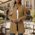 Woman wearing a camel colored button front midi coat with classic collar and A-line silhouette, standing in an outdoor cafe setting._0