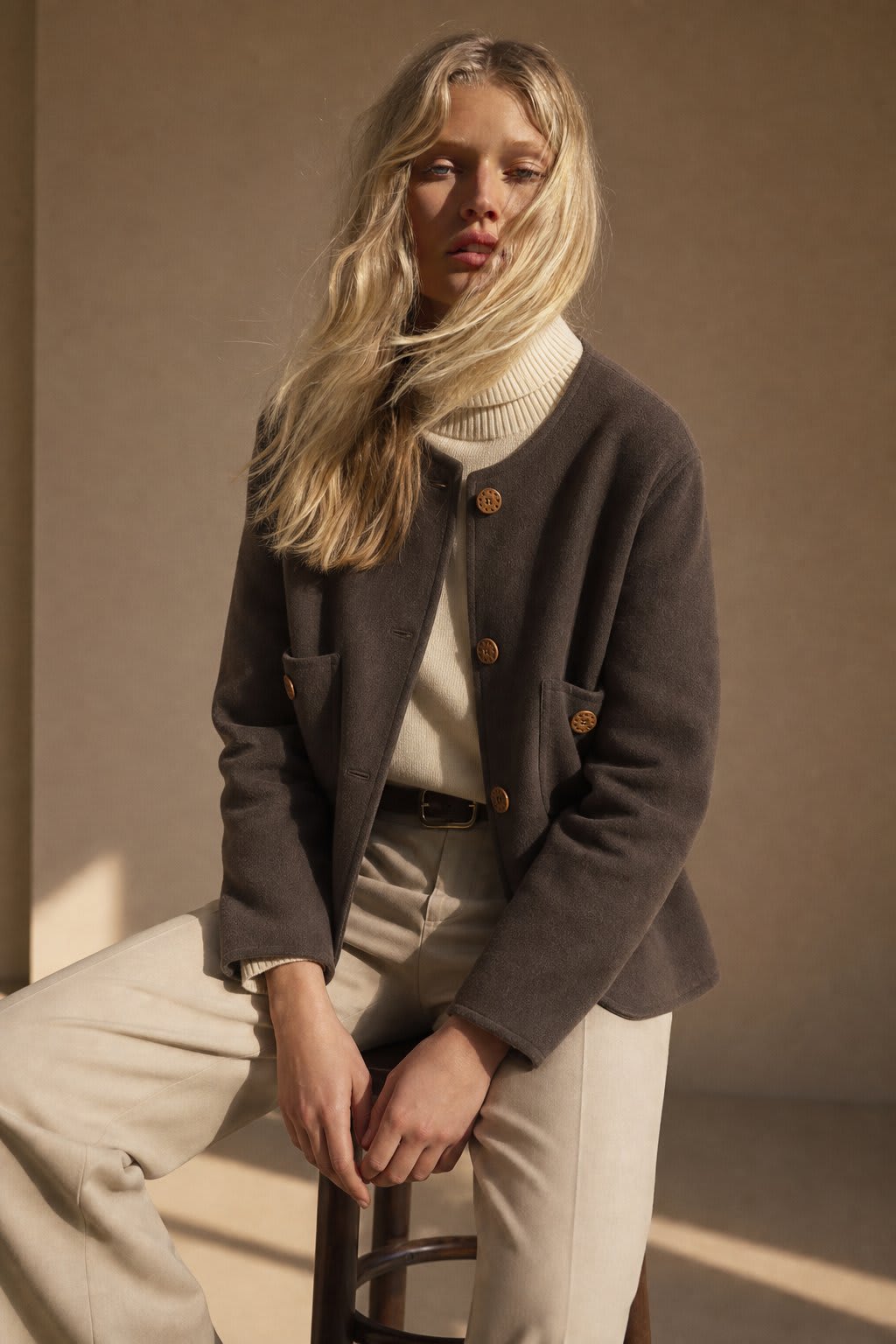Woman wearing a button-front jacket with round neckline over a turtleneck sweater and beige trousers in natural light_0