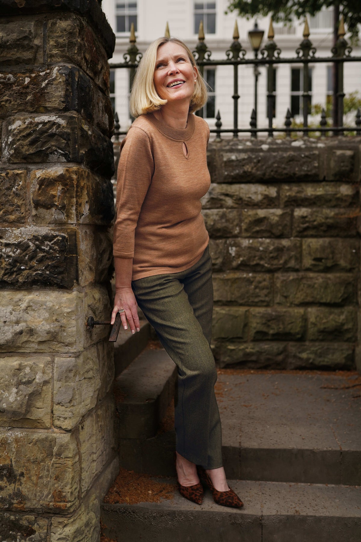 Woman wearing olive green straight-leg trousers with a beige knit top and leopard print pointed heels on stone steps._2