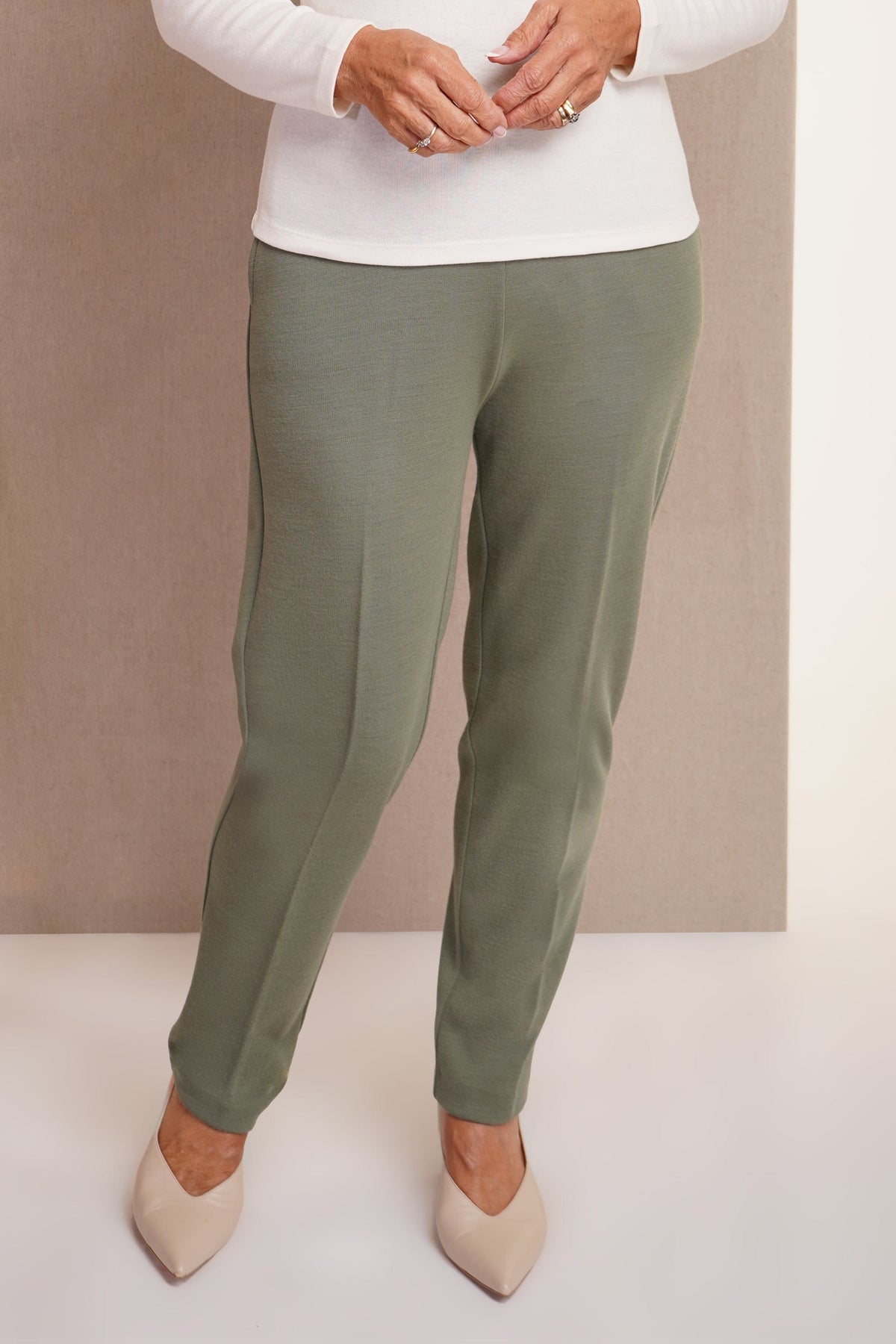 Woman wearing sage green high-waisted tapered trousers with a white long-sleeve top and cream pointed heels._0