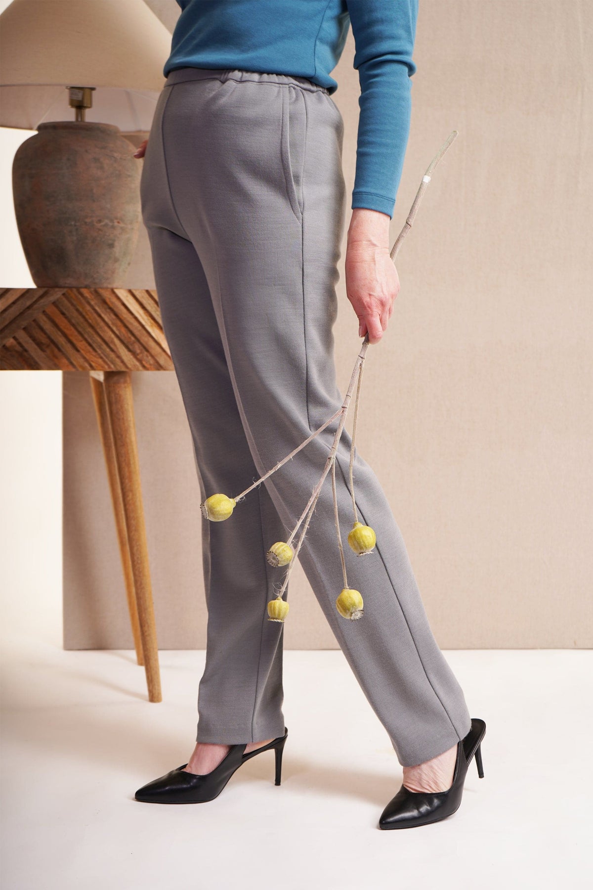 Woman wearing grey straight-leg trousers with a front seam, a teal top and black pointed heels._1