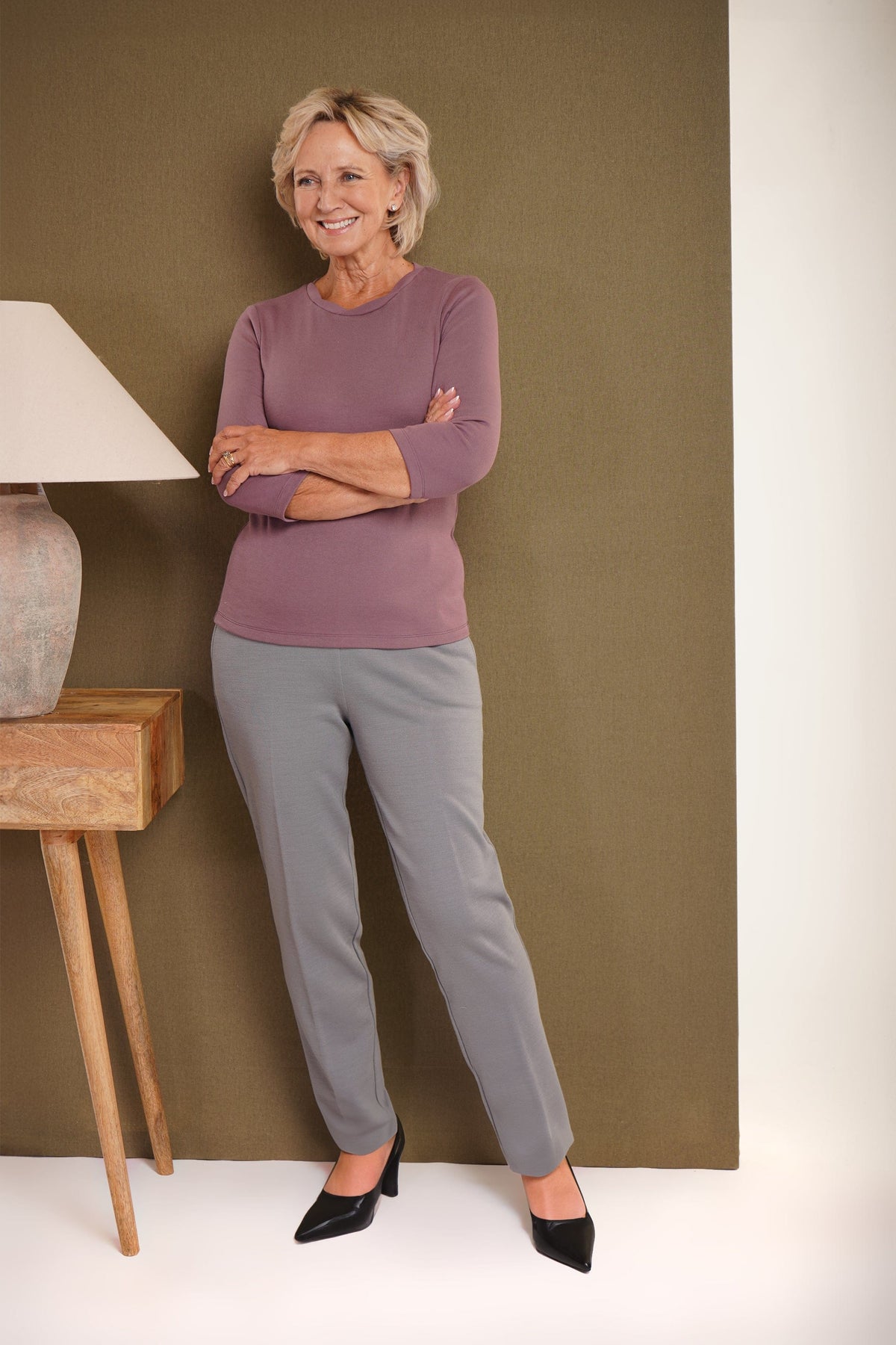 Woman wearing grey straight-leg trousers with a front seam, a teal top and black pointed heels._2