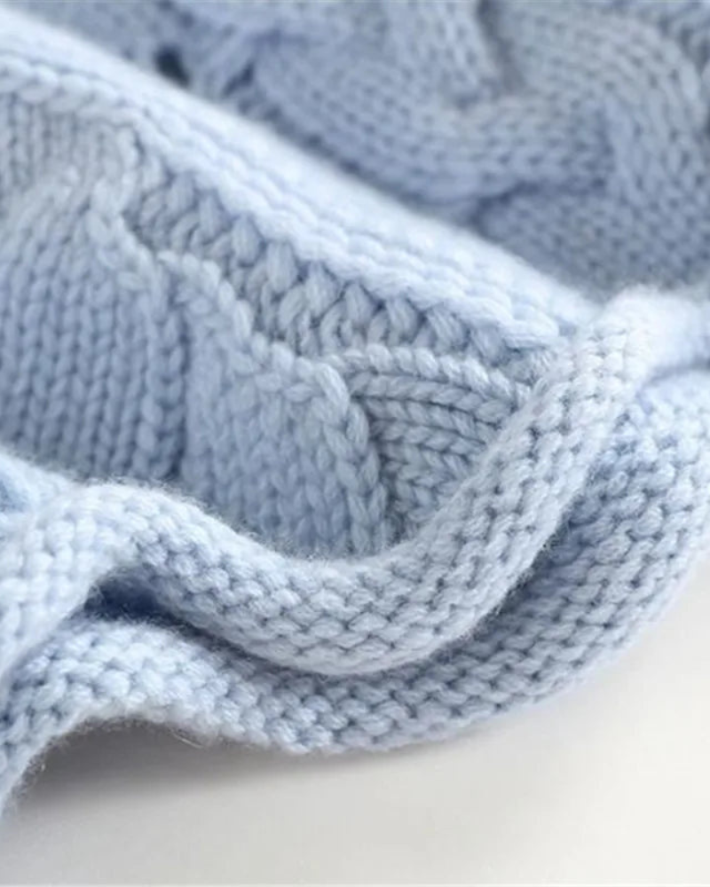 Close-up of the sweater’s pale blue cable-knit texture, showing raised braided stitches and ribbed knit detail.