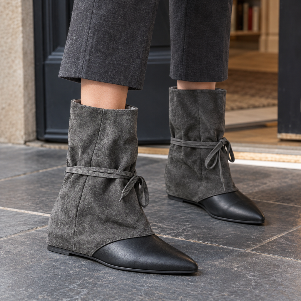 Grey slouched ankle boots with black pointed toes and wrap-around ties, worn with grey wide-leg trousers on a stone pavement._0