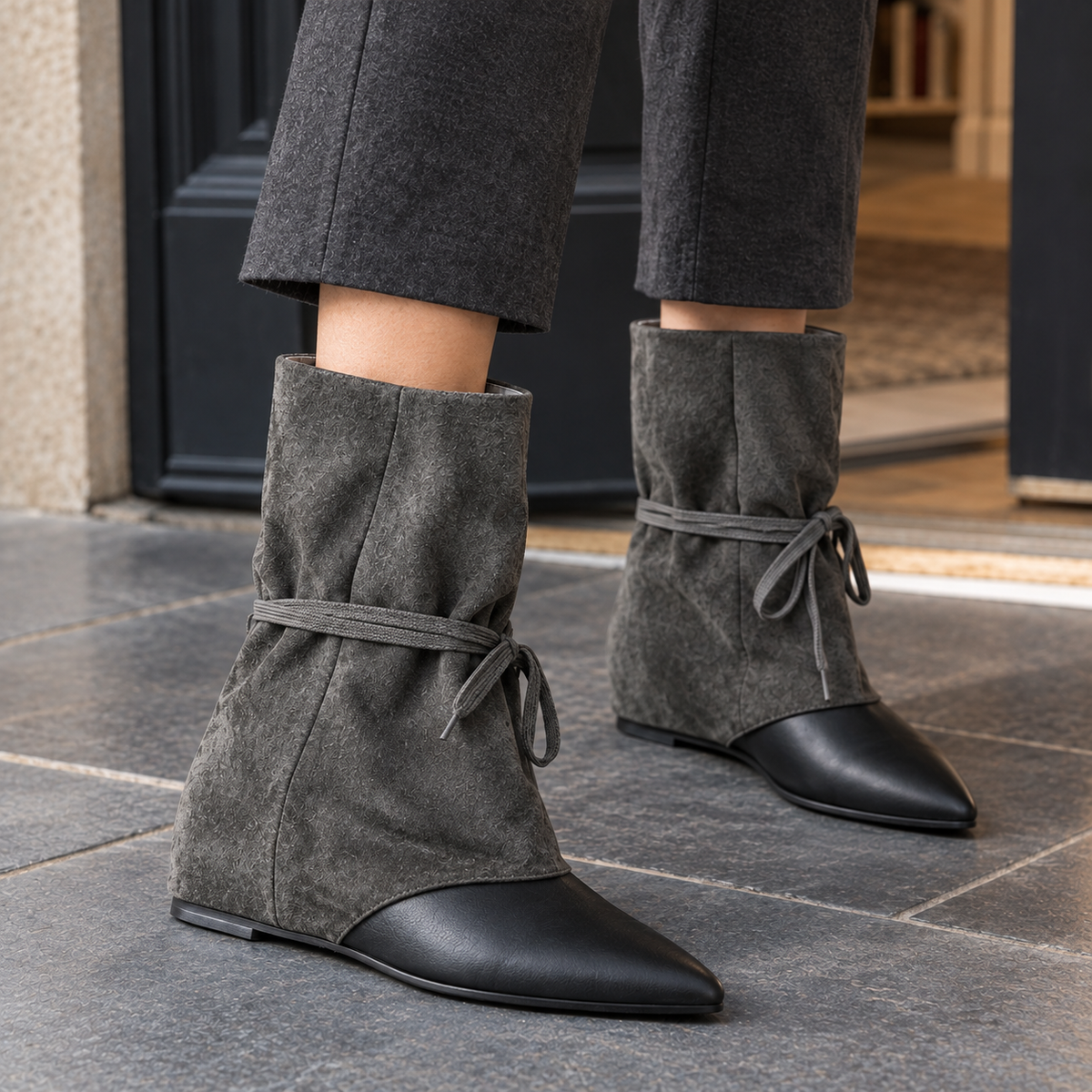 Grey slouched ankle boots with black pointed toes and wrap-around ties, worn with grey wide-leg trousers on a stone pavement._1