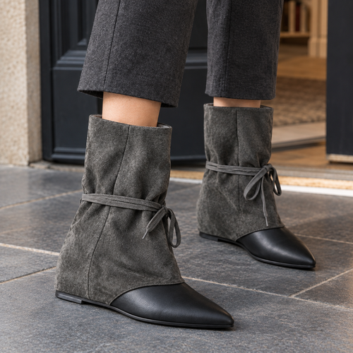 Grey slouched ankle boots with black pointed toes and wrap-around ties, worn with grey wide-leg trousers on a stone pavement._1