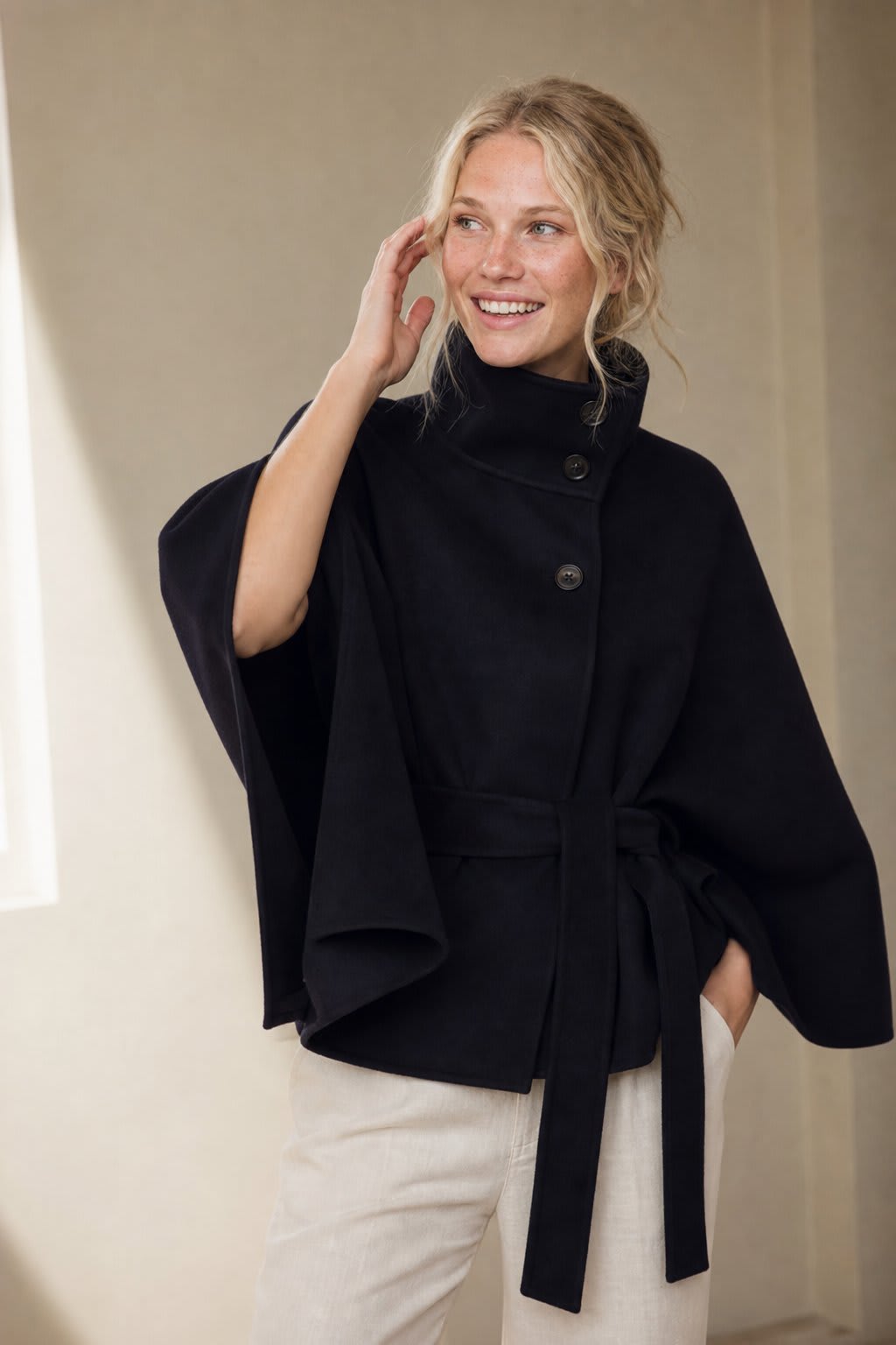 Woman wearing a short cape coat with stand collar, button details, and belted waist._0