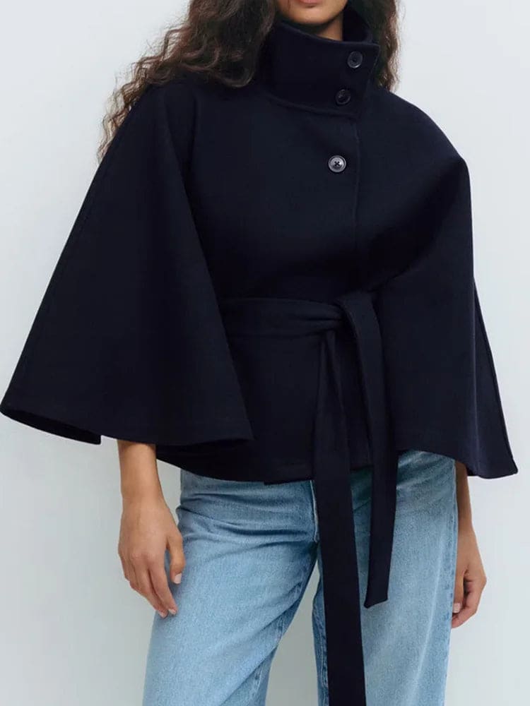 Woman wearing a short cape coat with stand collar, button details, and belted waist._10