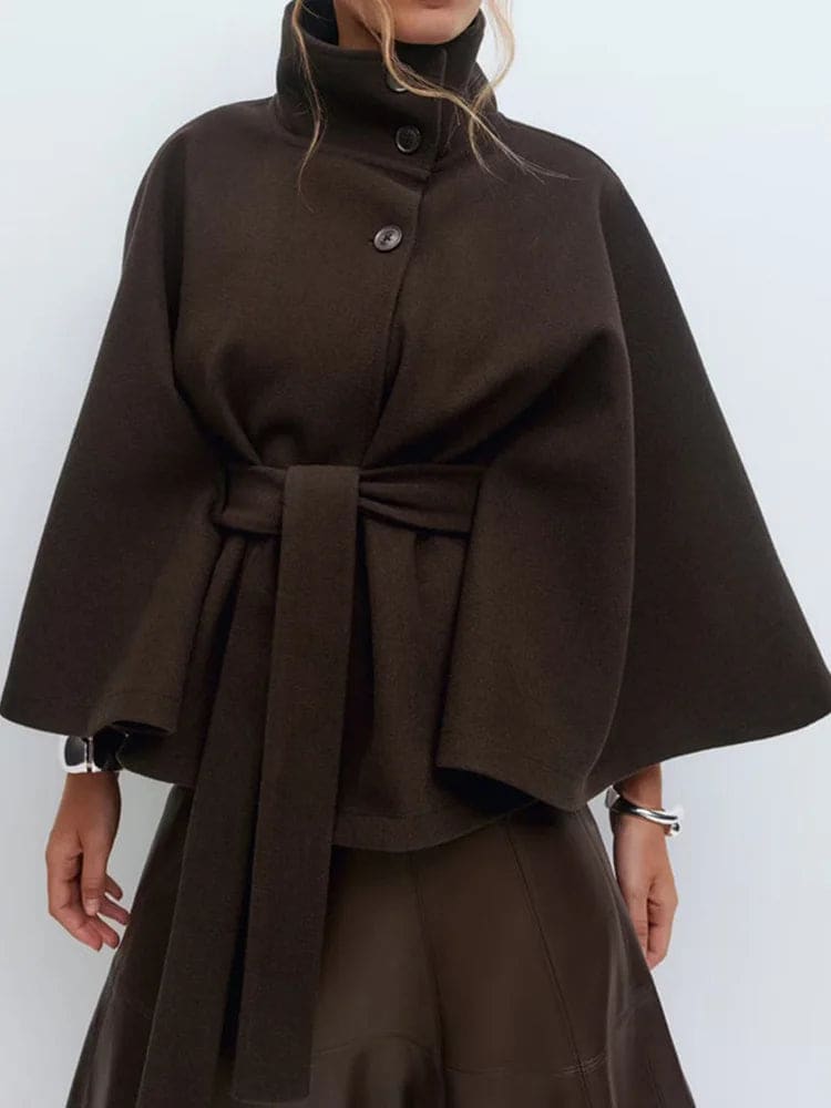Woman wearing a short cape coat with stand collar, button details, and belted waist._11