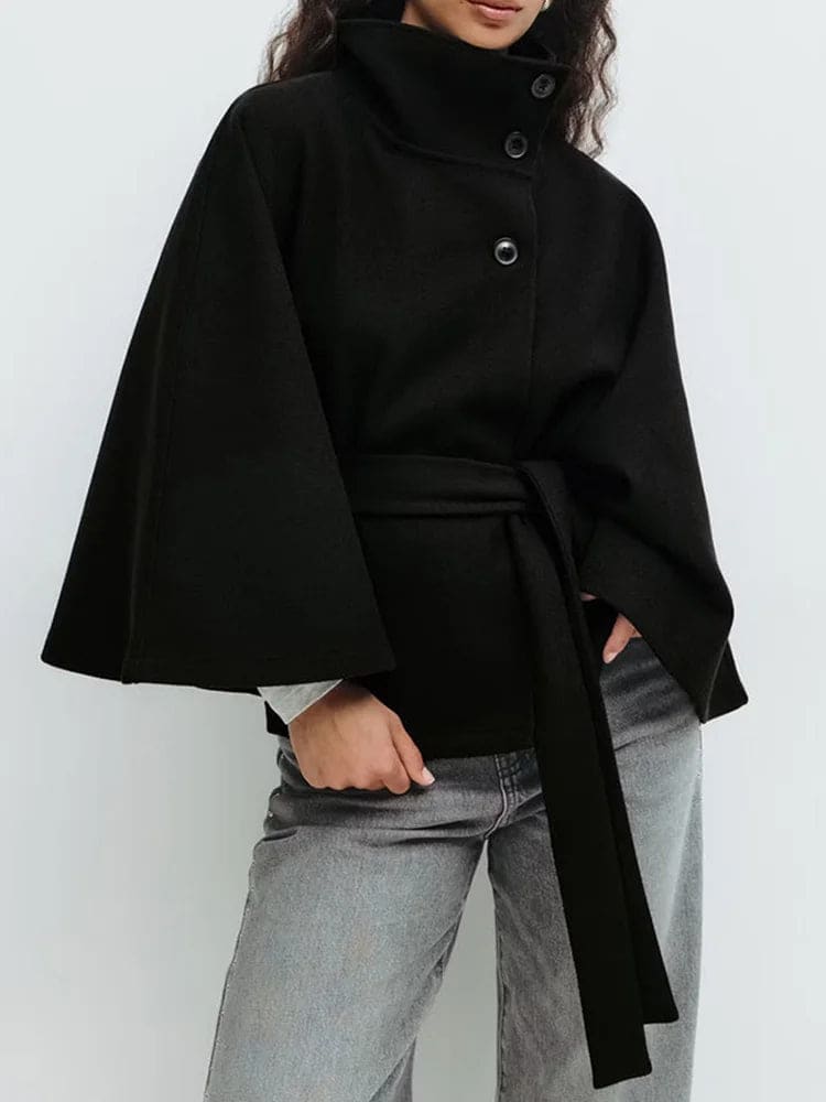 Woman wearing a short cape coat with stand collar, button details, and belted waist._12