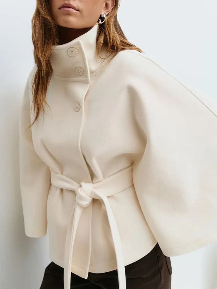 Woman wearing a short cape coat with stand collar, button details, and belted waist._13