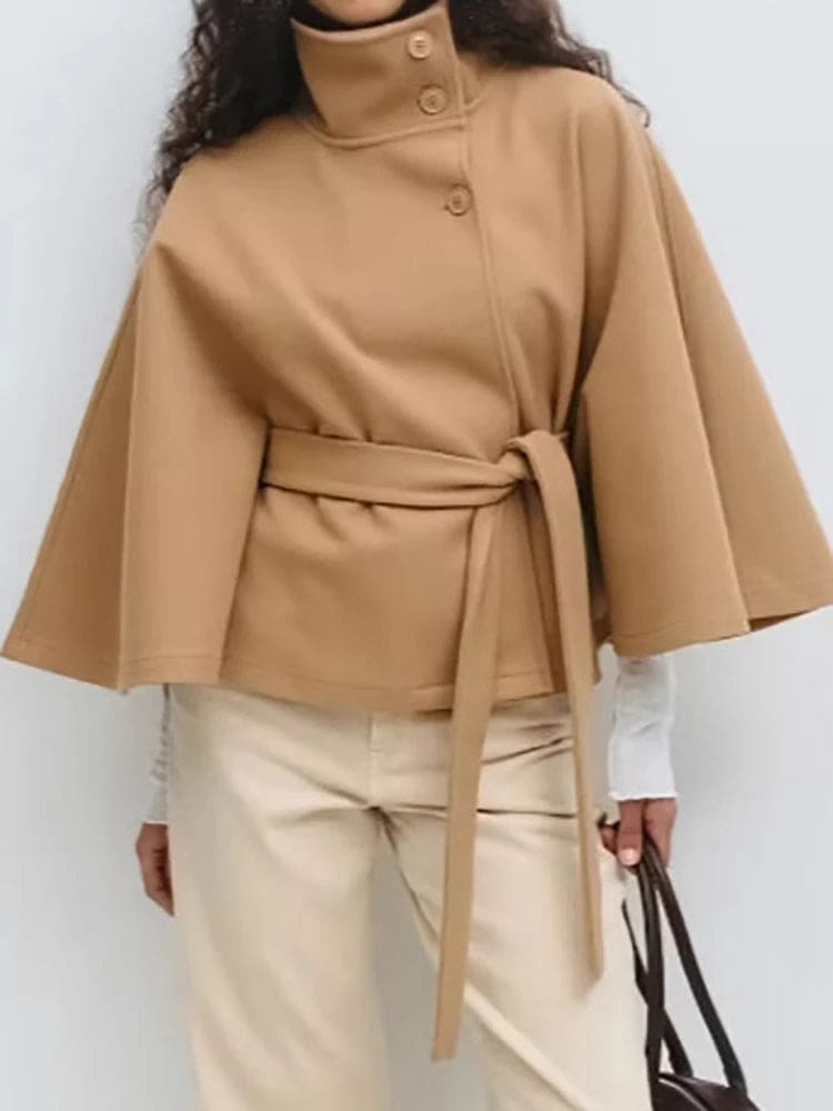 Woman wearing a short cape coat with stand collar, button details, and belted waist._14