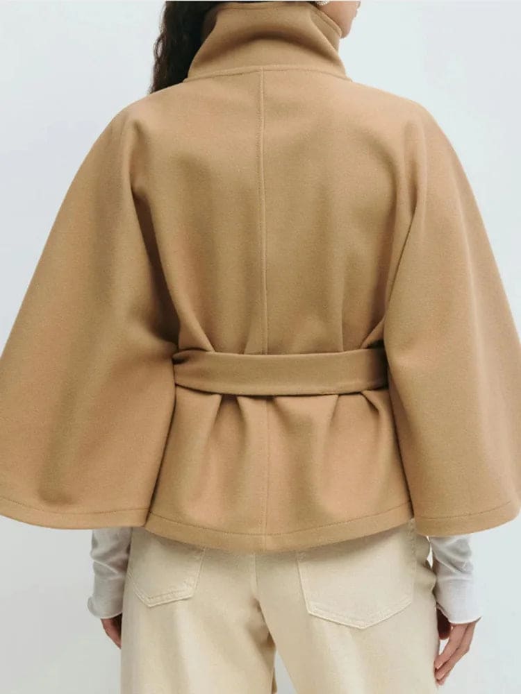 Woman wearing a short cape coat with stand collar, button details, and belted waist._15