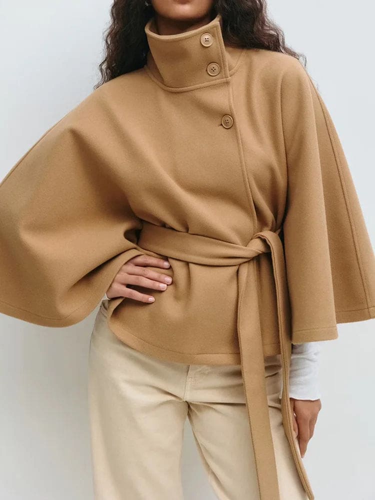 Woman wearing a short cape coat with stand collar, button details, and belted waist._16