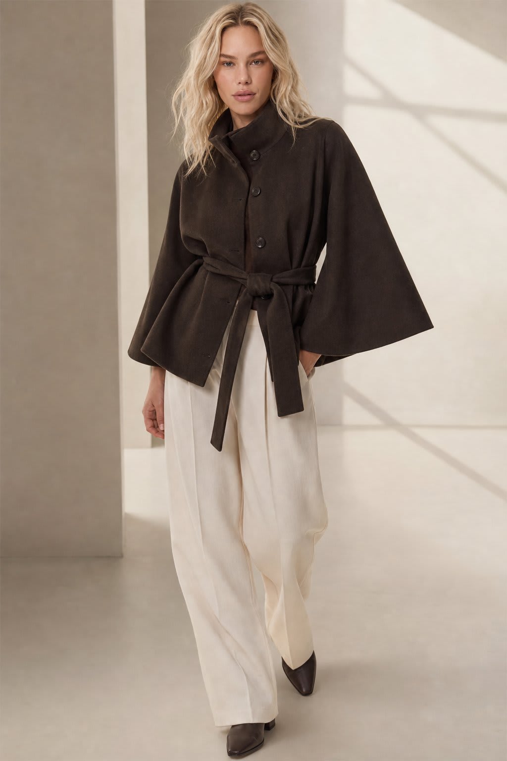 Woman wearing a short cape coat with stand collar, button details, and belted waist._2