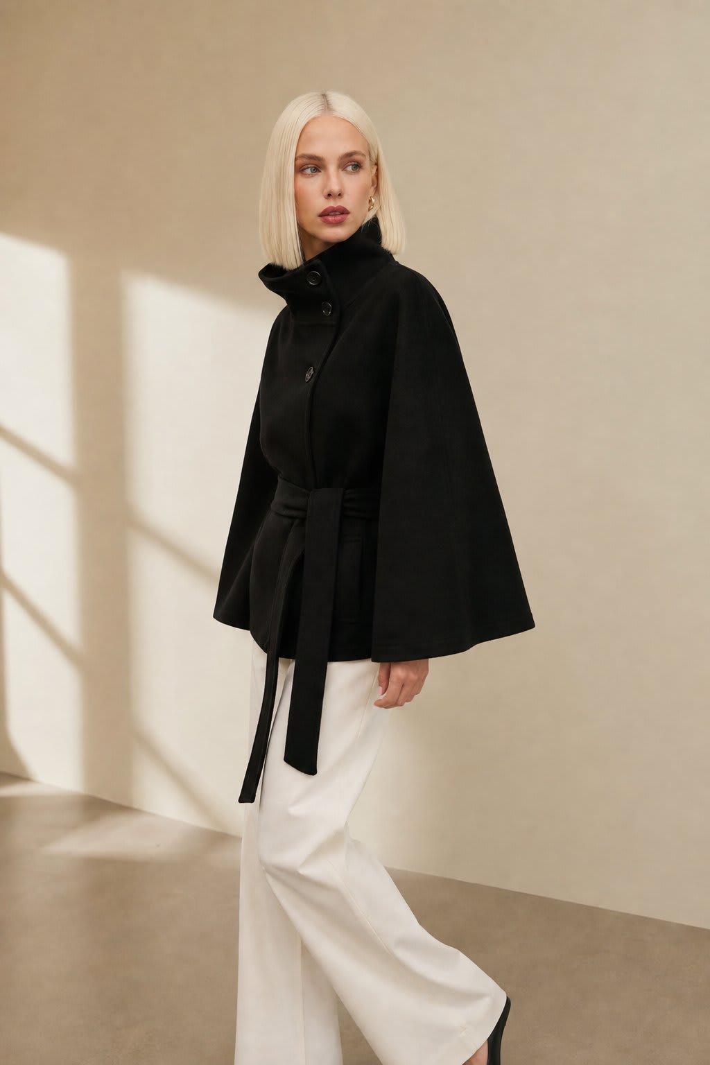 Woman wearing a short cape coat with stand collar, button details, and belted waist._4