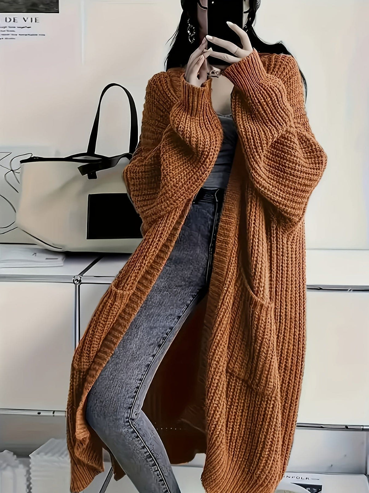 Woman wearing a longline chunky knit cardigan with button front, styled over a layered outfit with a crossbody bag._11